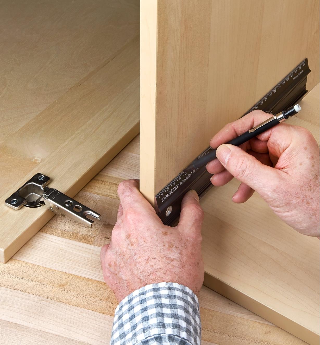 Using a pencil and a shop rule to mark hinge locations on an inside cabinet wall