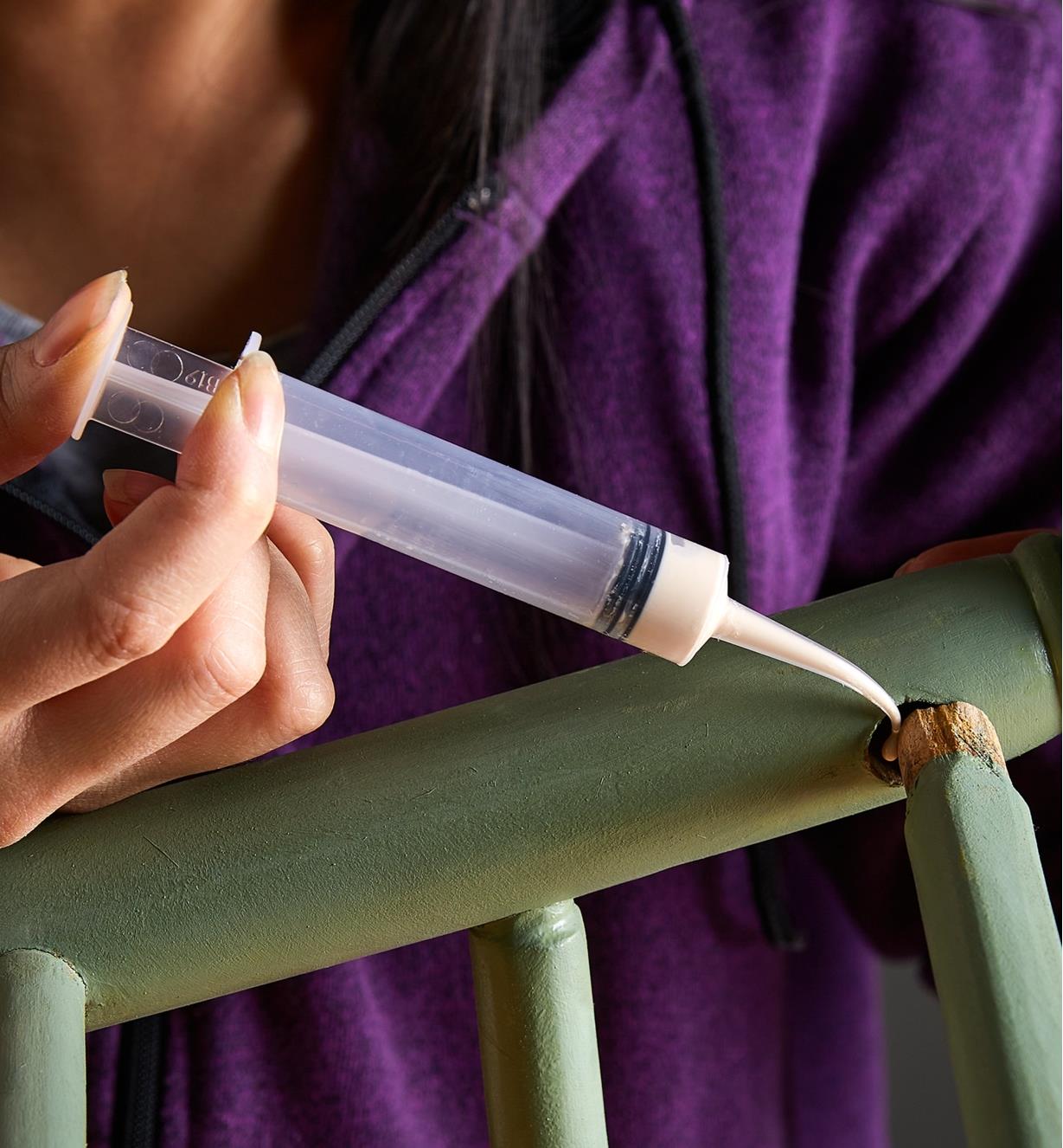 A curved-tip syringe is used to apply glue to the back of a chair