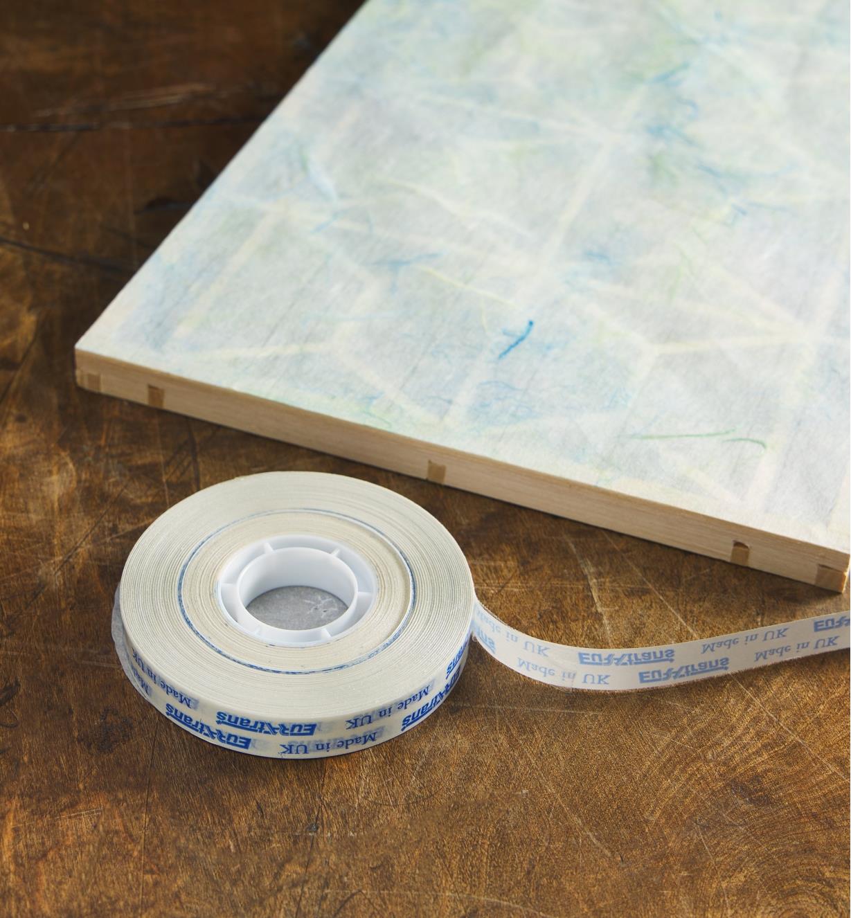 A roll of transfer tape in front of a wood panel