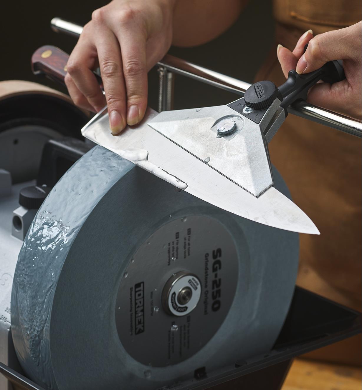 A wide knife jig holds a large knife blade being sharpened on a wheel