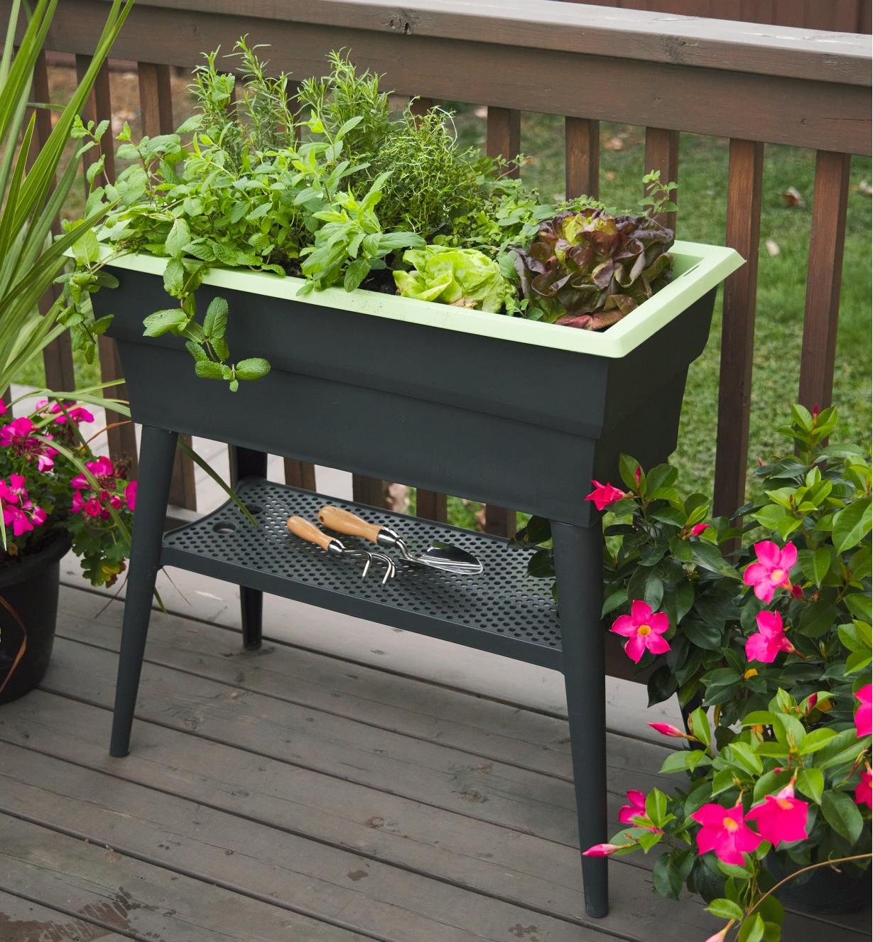 The self-watering raised planter filled with growing plants sits on a deck  