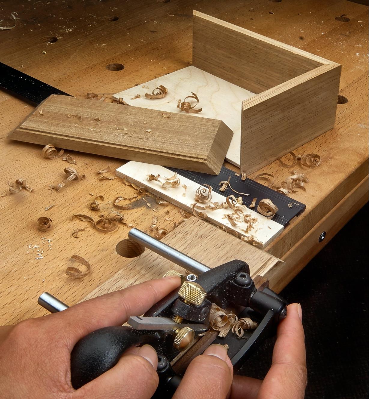 Using a box-maker’s plow plane to cut a groove in the wall of a wooden box to hold the box bottom
