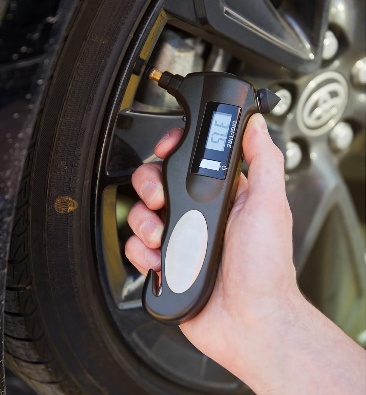 Personne vérifiant la pression d’un pneu de voiture à l’aide d’un manomètre numérique pour pneus