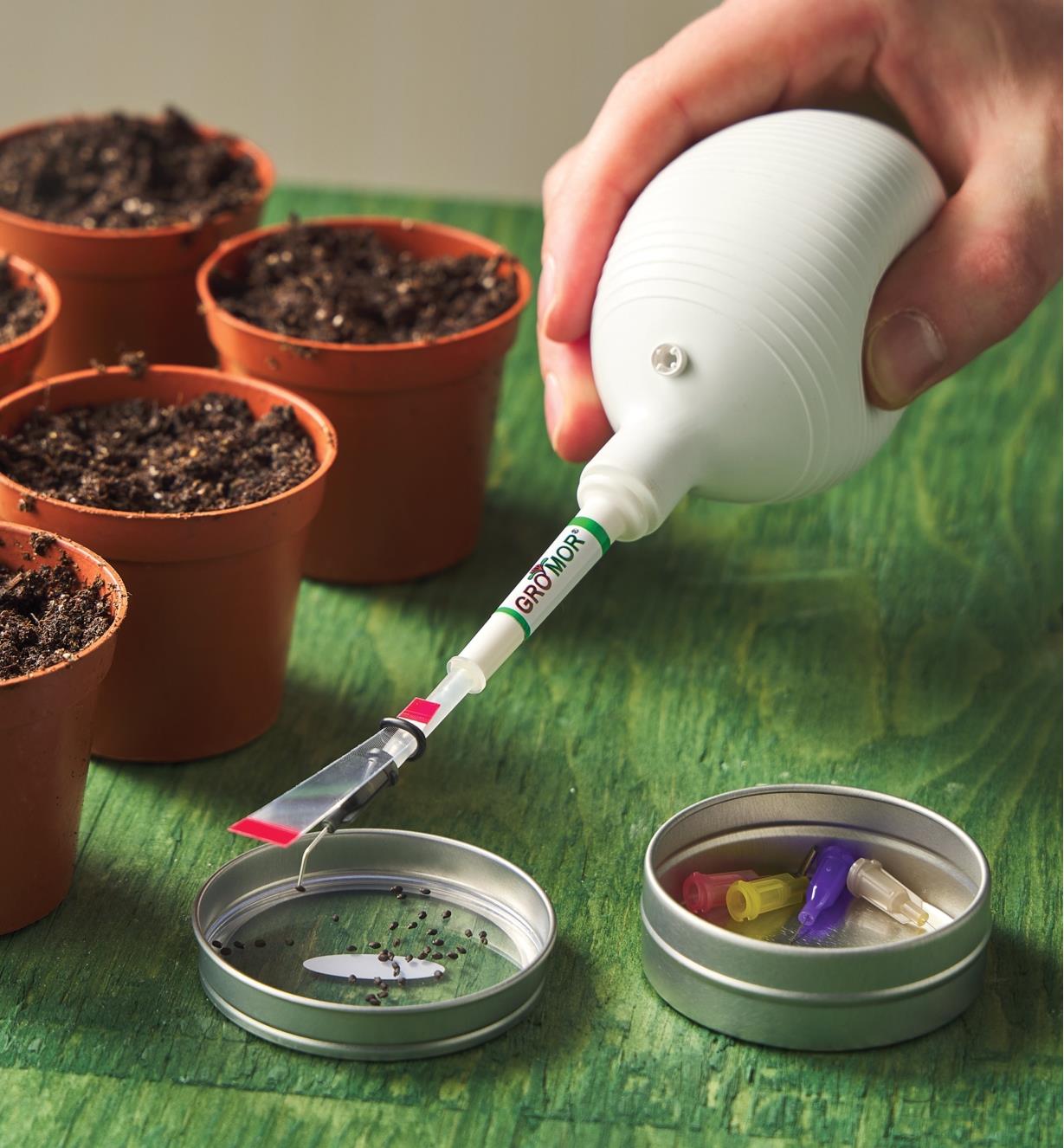 Using a mini wand seeder with a magnifier to pick up a tiny seed next to pots of soil