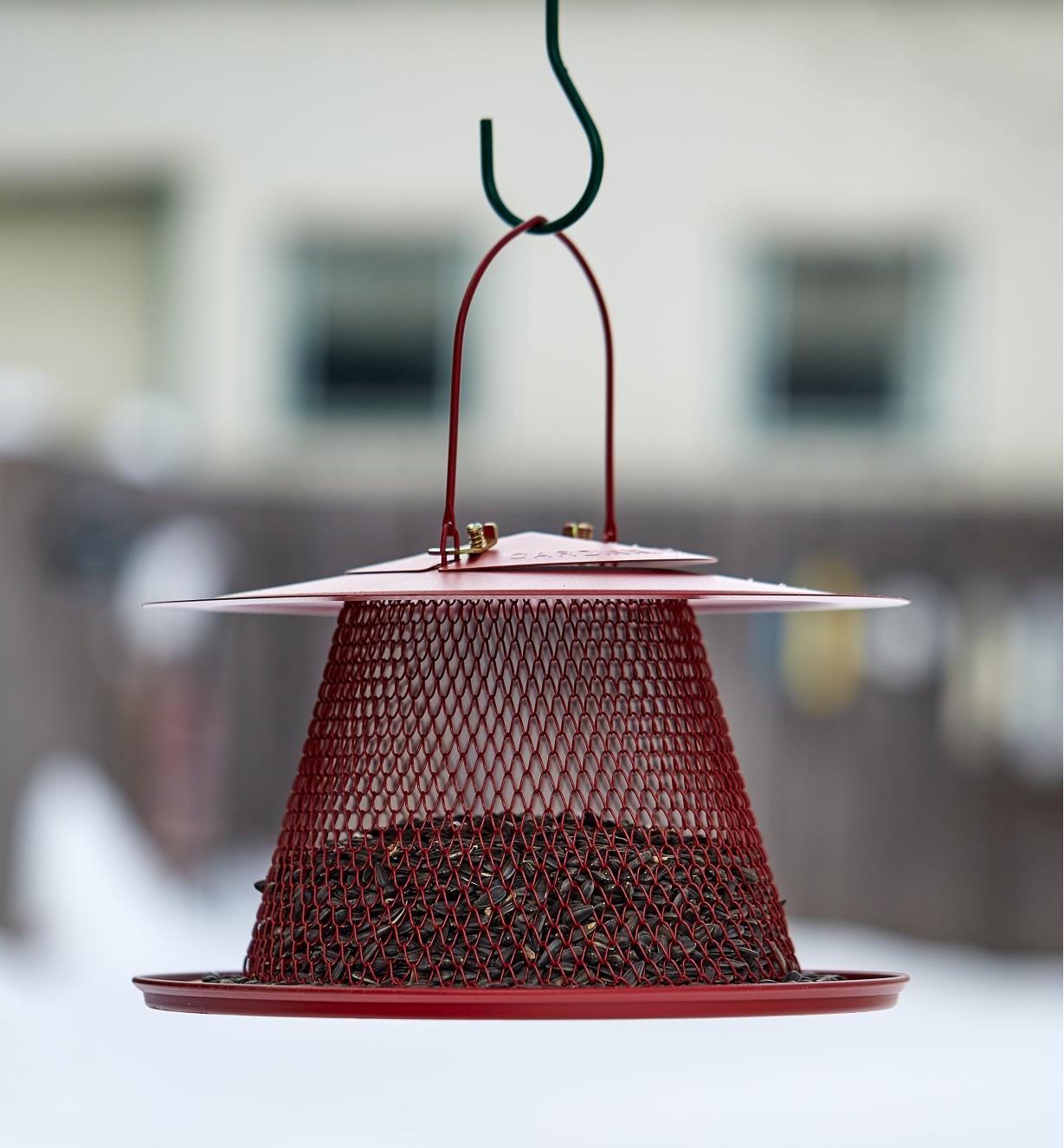 A collapsible bird feeder half full of seeds hangs from a hook outdoors