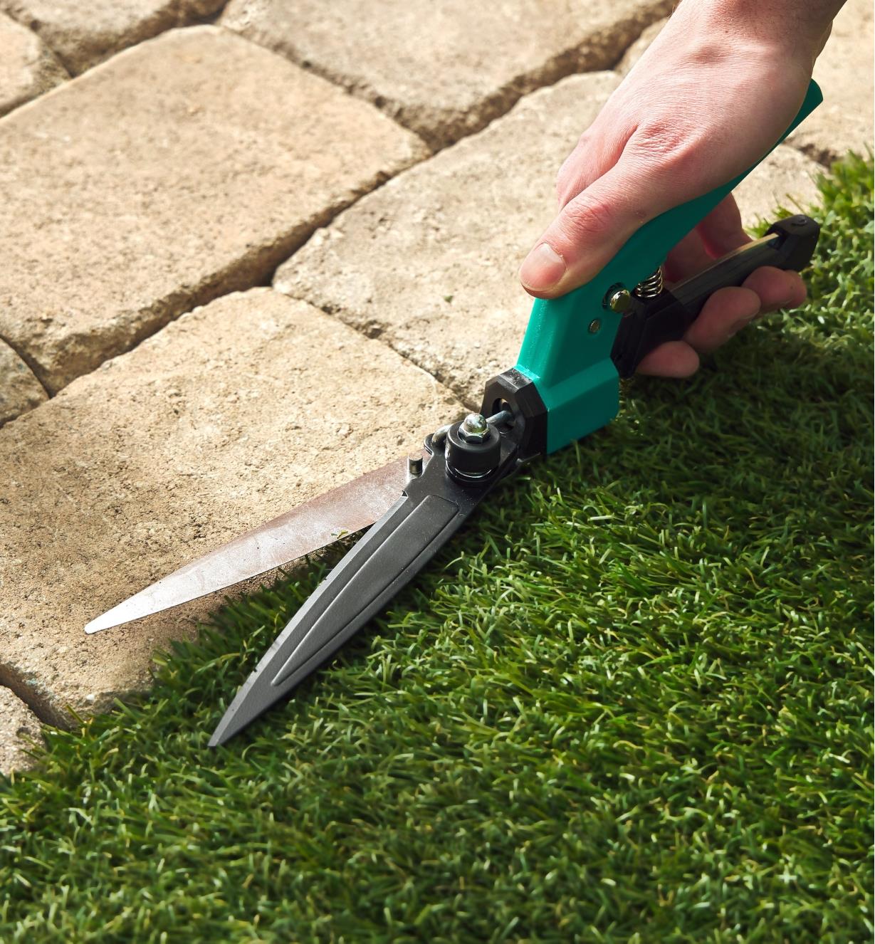 Using adjustable grass shears to trim grass beside patio stones