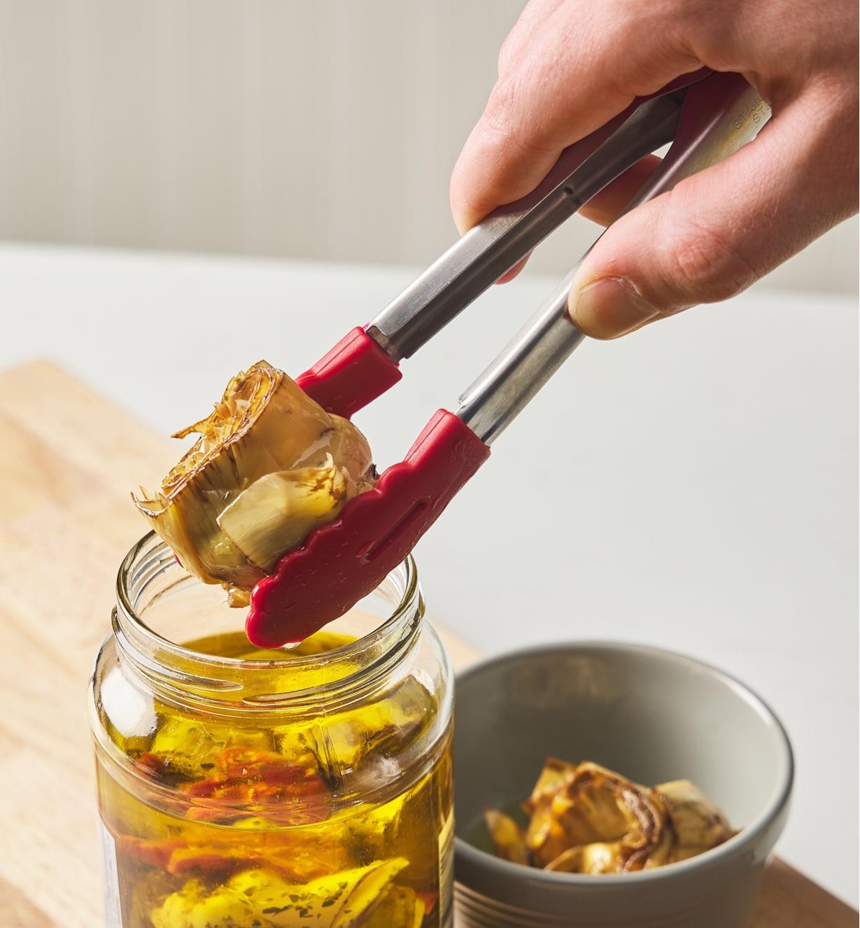 Using mini tongs to remove an artichoke heart from a jar