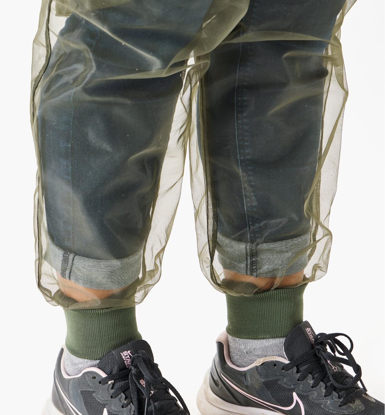 Vue rapprochée des bords-côtes d'un pantalon antimoustiques porté par-dessus un jean