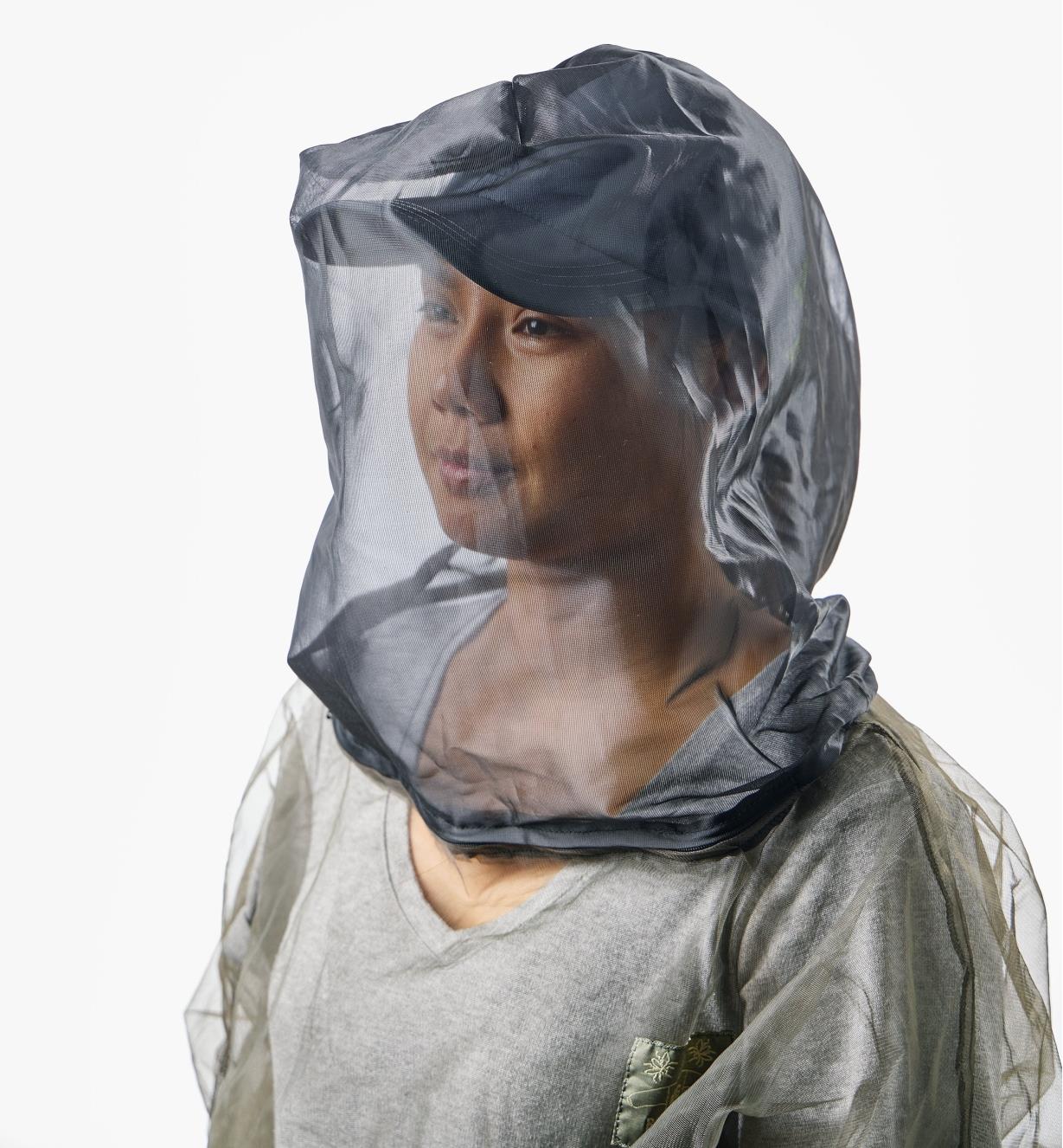 A woman wears a hooded bug-protection shirt with a baseball cap underneath