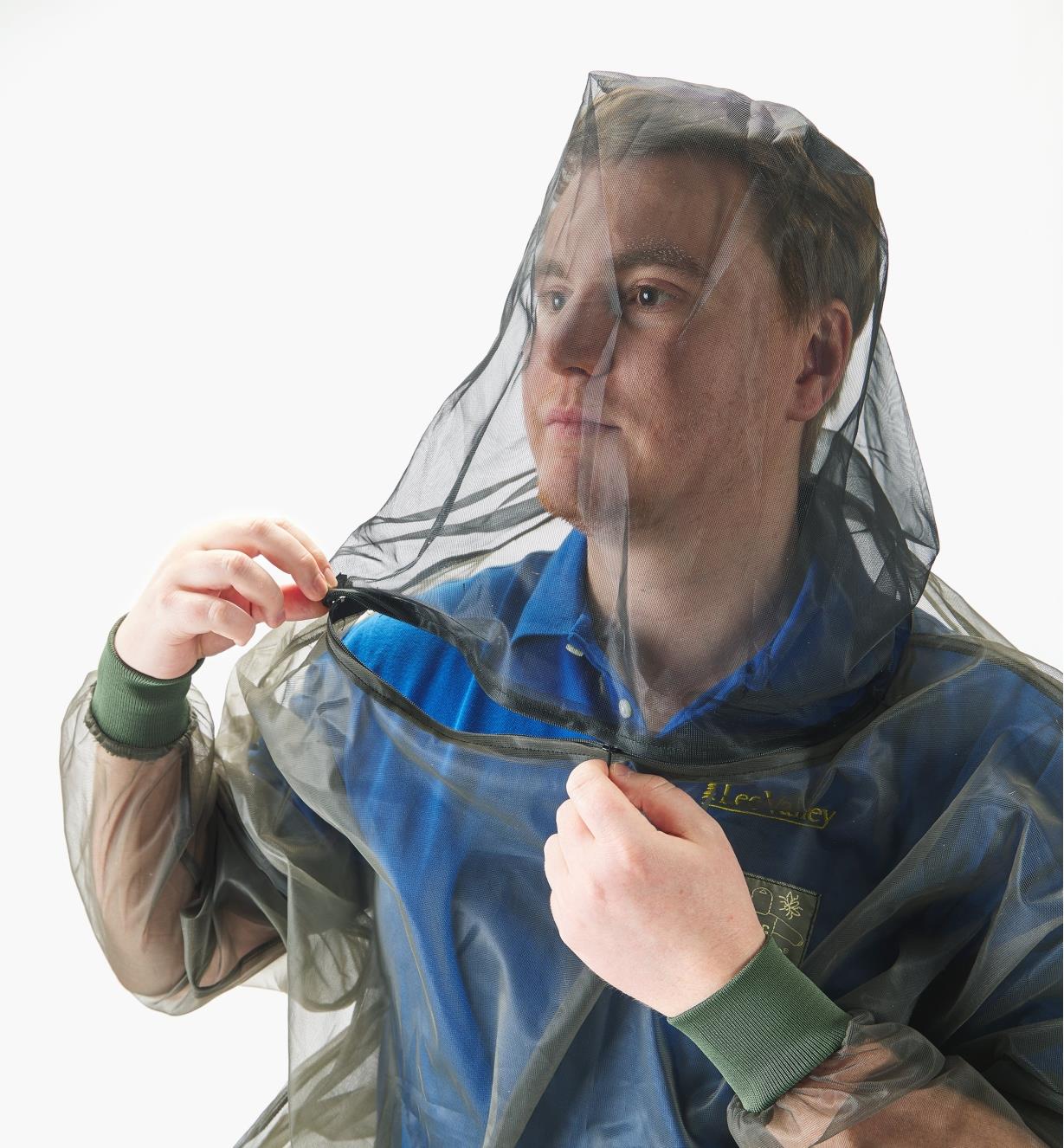 A man wearing a hooded bug-protection shirt opens a zipper at the neck
