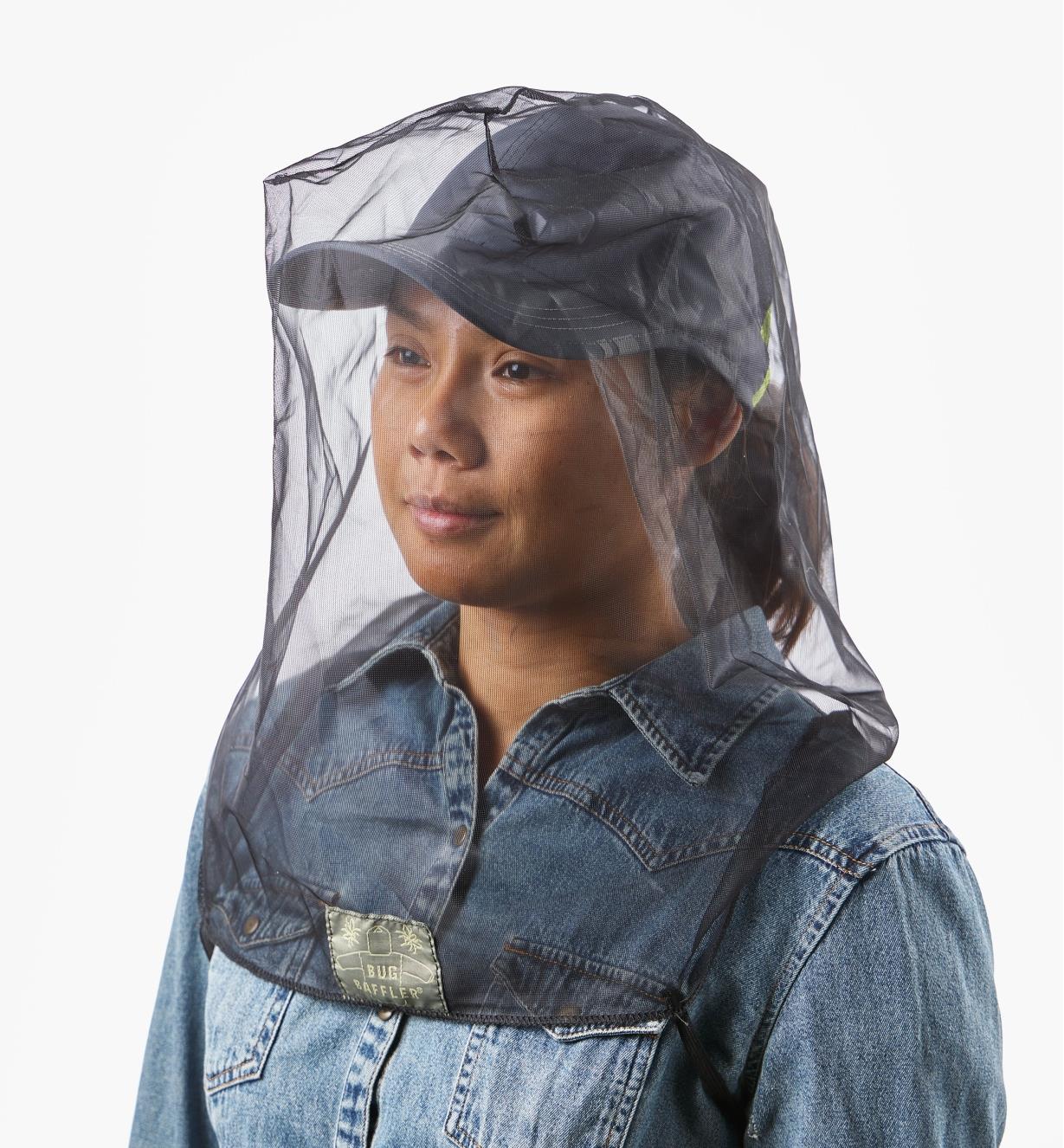 A woman wearing a baseball cap with a bug-protection hood worn over it