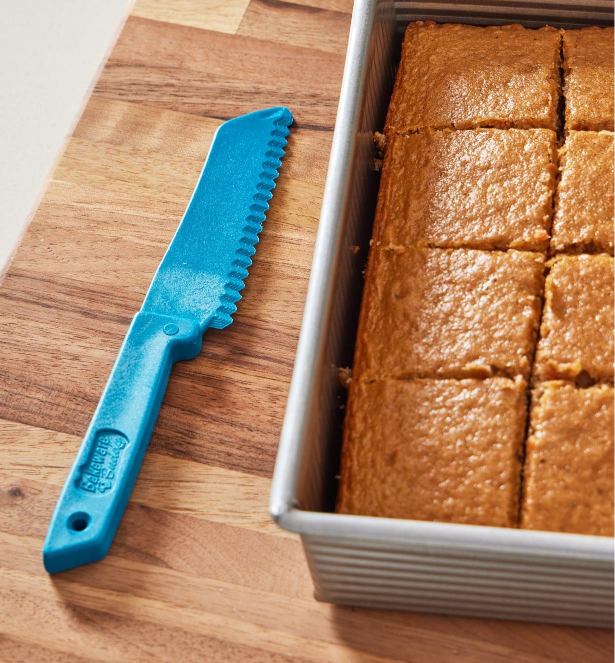 The bakeware buddy knife resting beside a cake cut in portions in a non-stick pan