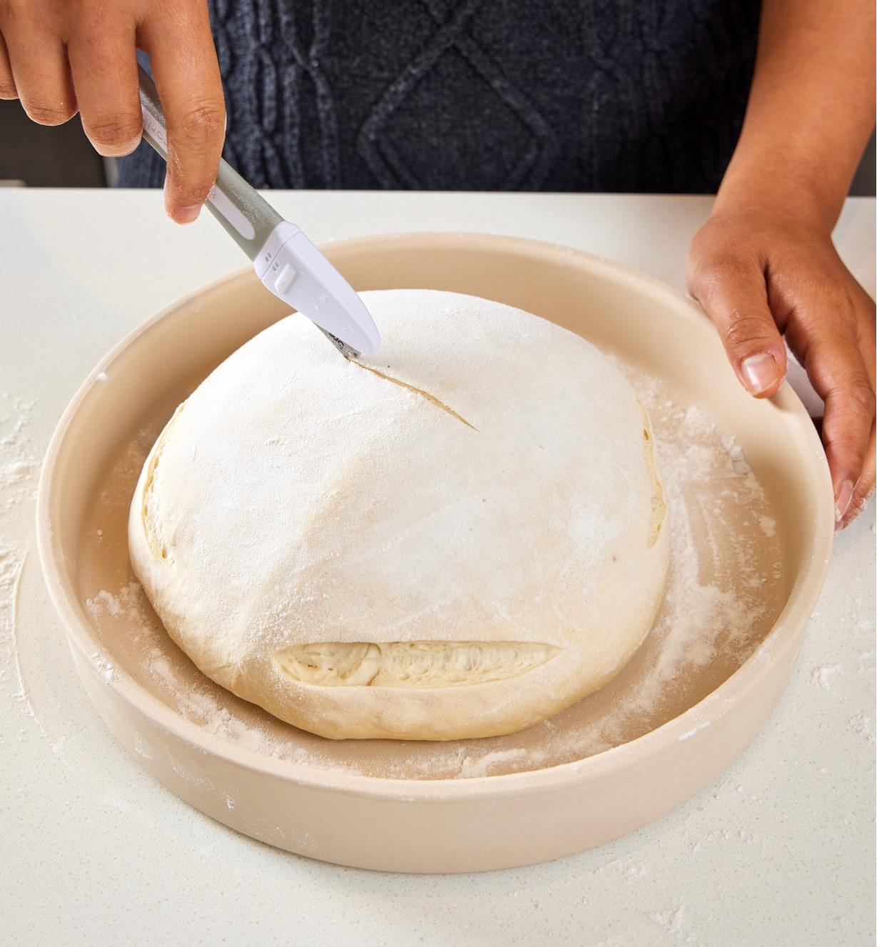 Scoring the top of dough in the base of the bread-baking cloche