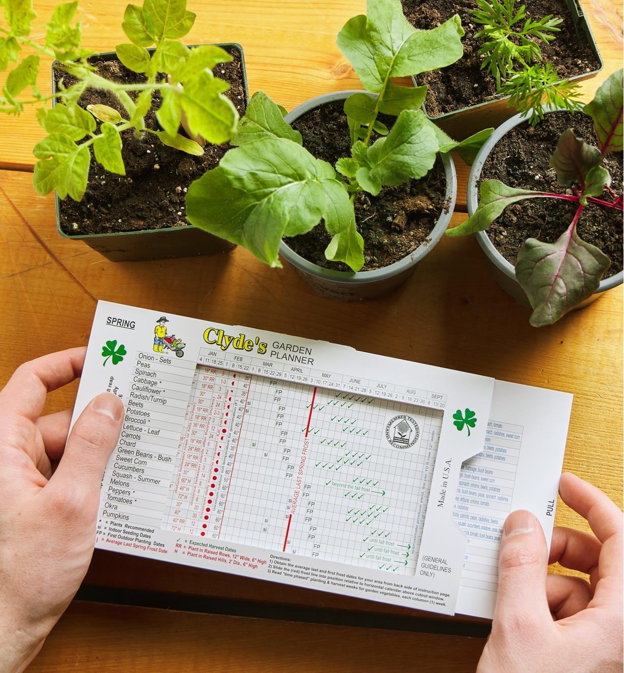 Pulling out the sliding chart of the vegetable garden planner, with several small potted plants in the background