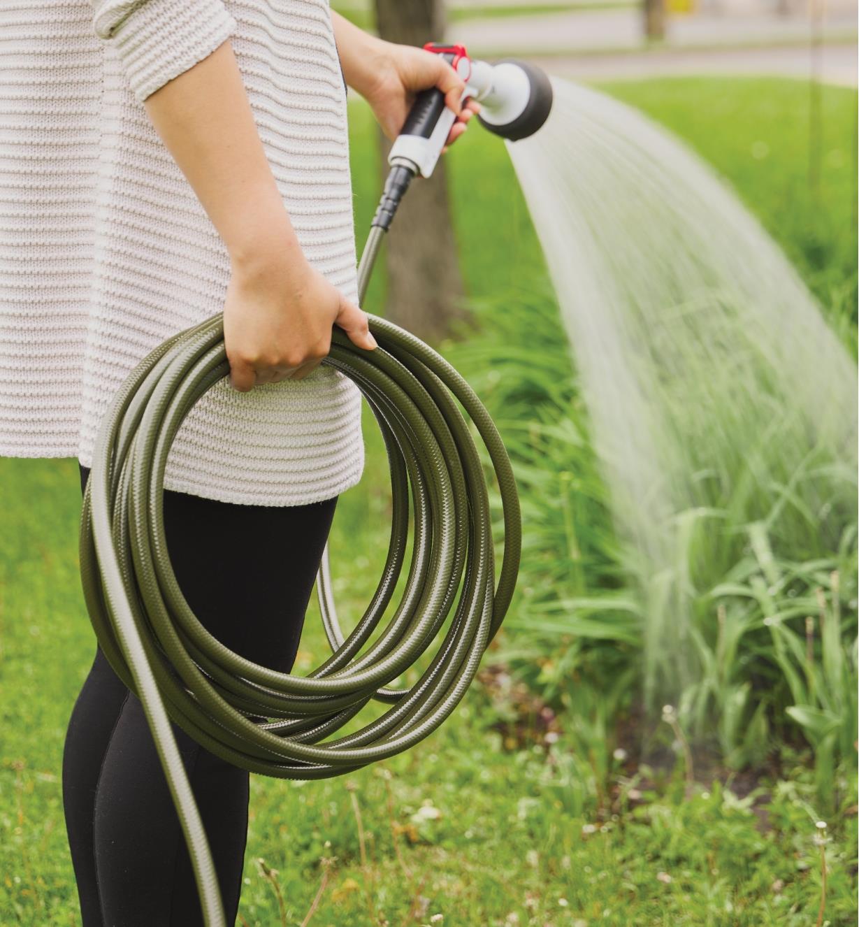 A person holds a coiled lightweight hose with attached sprayer while watering garden plants