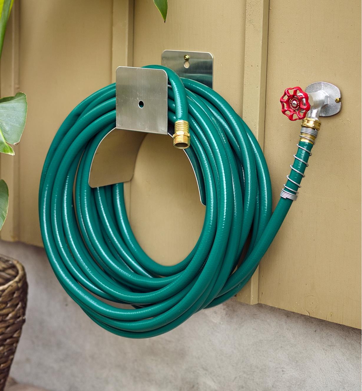 A hose connected to a tap and coiled around a hose hanger on the side of a house