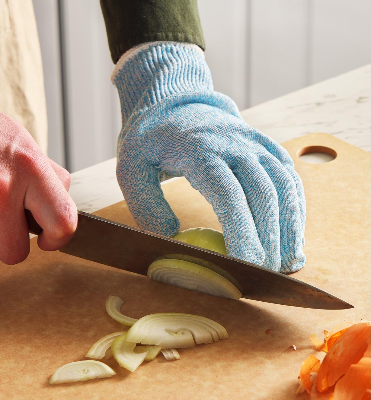 A gloved hand holds an onion in place on a cutting board as it is being sliced