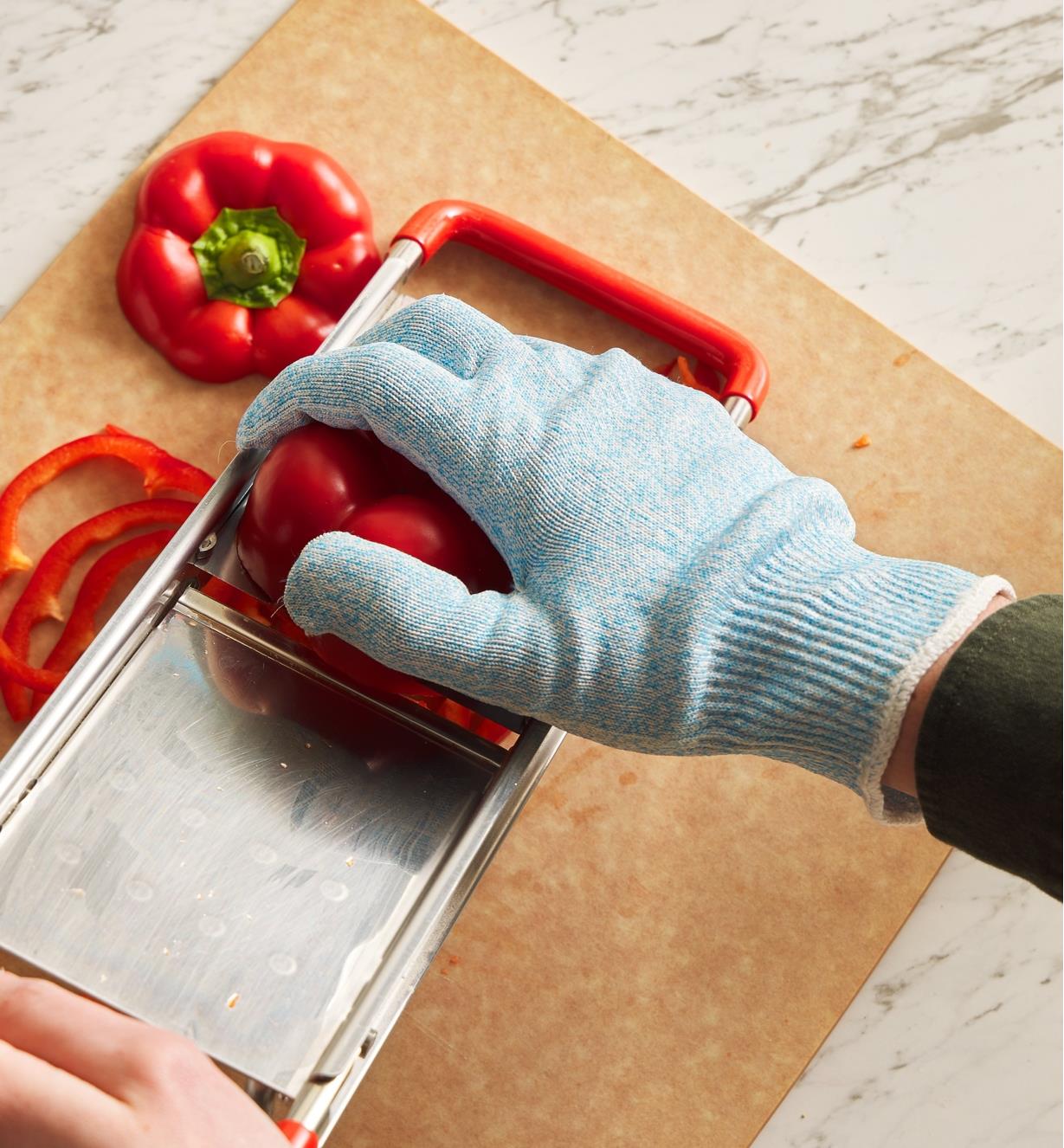 A gloved hand slices a red pepper on a mandoline