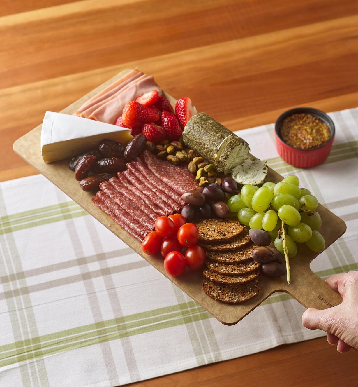 A cut & serve board with charcuterie on it, being placed on a table