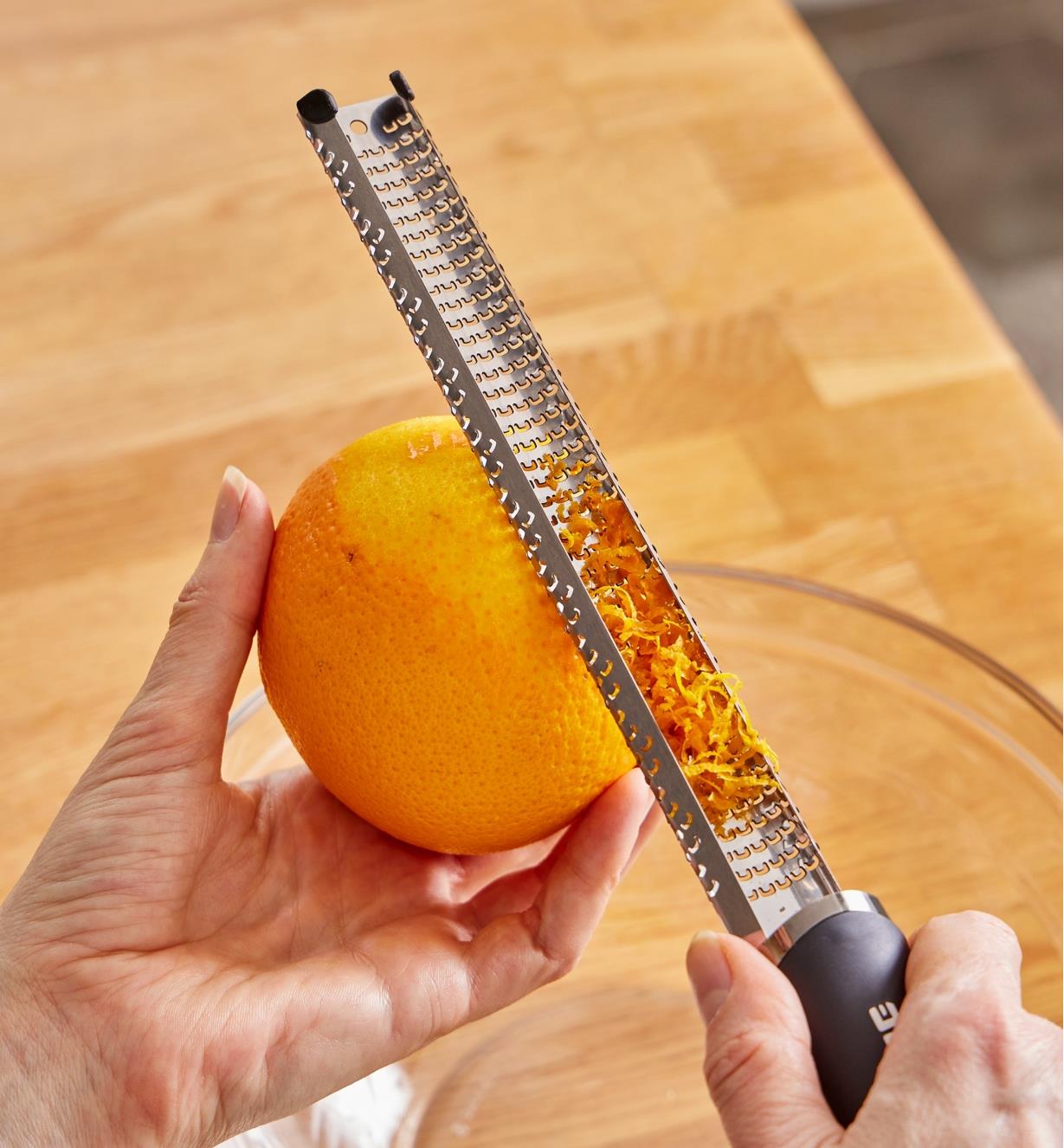 Personne zestant une orange à l'aide d'un zesteur en acier inoxydable avec poignée