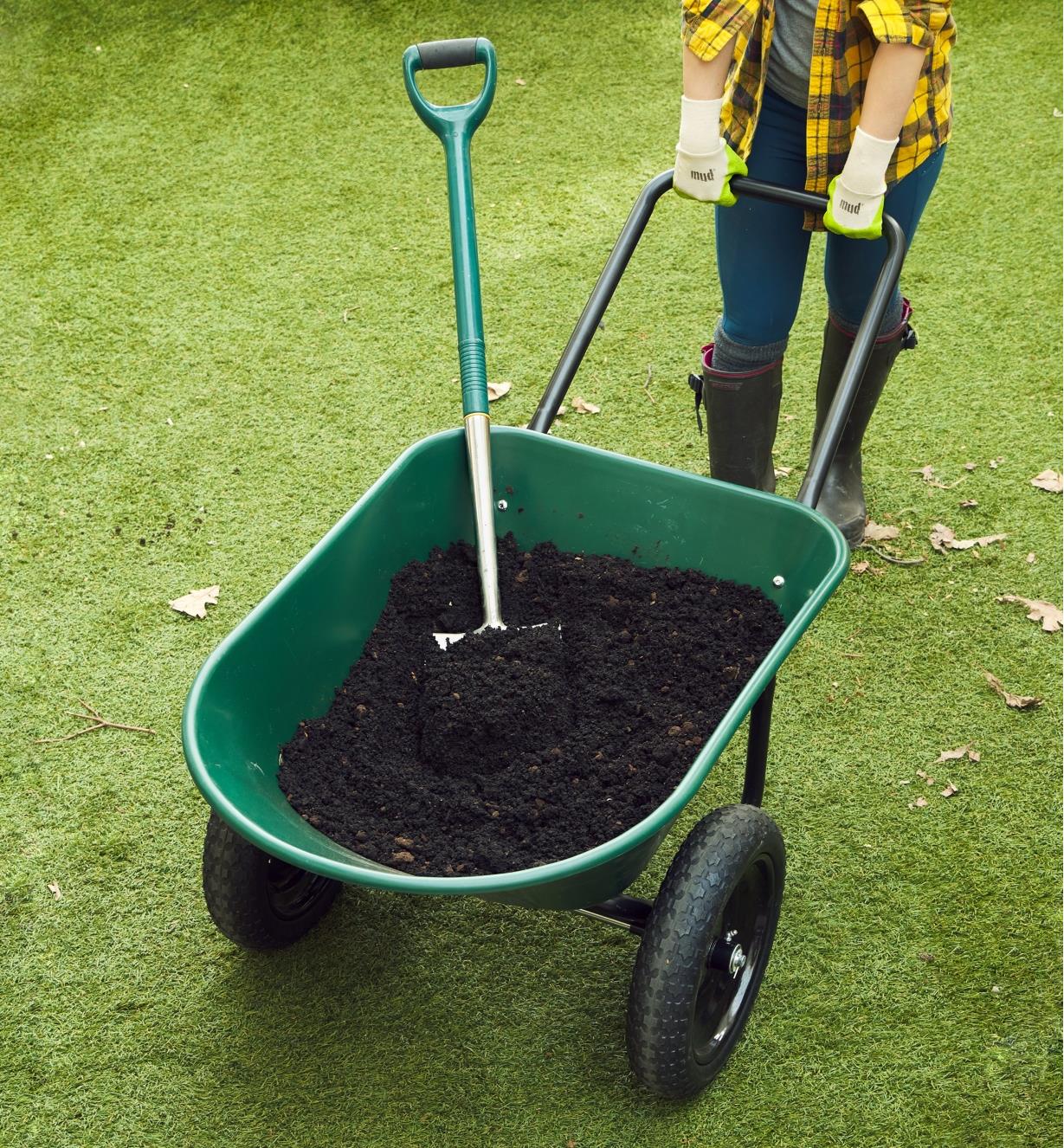 The wheelbarrow with flat-free tires filled with garden soil and a shovel