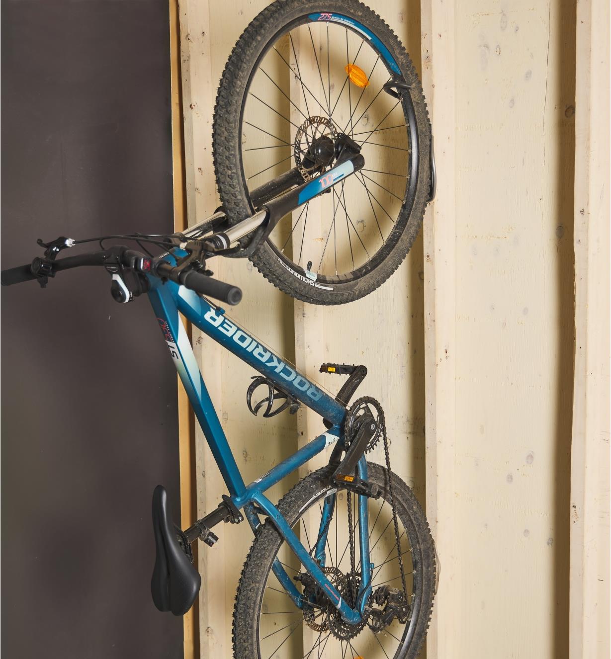 A bicycle suspended vertically against a wall on a bicycle rack