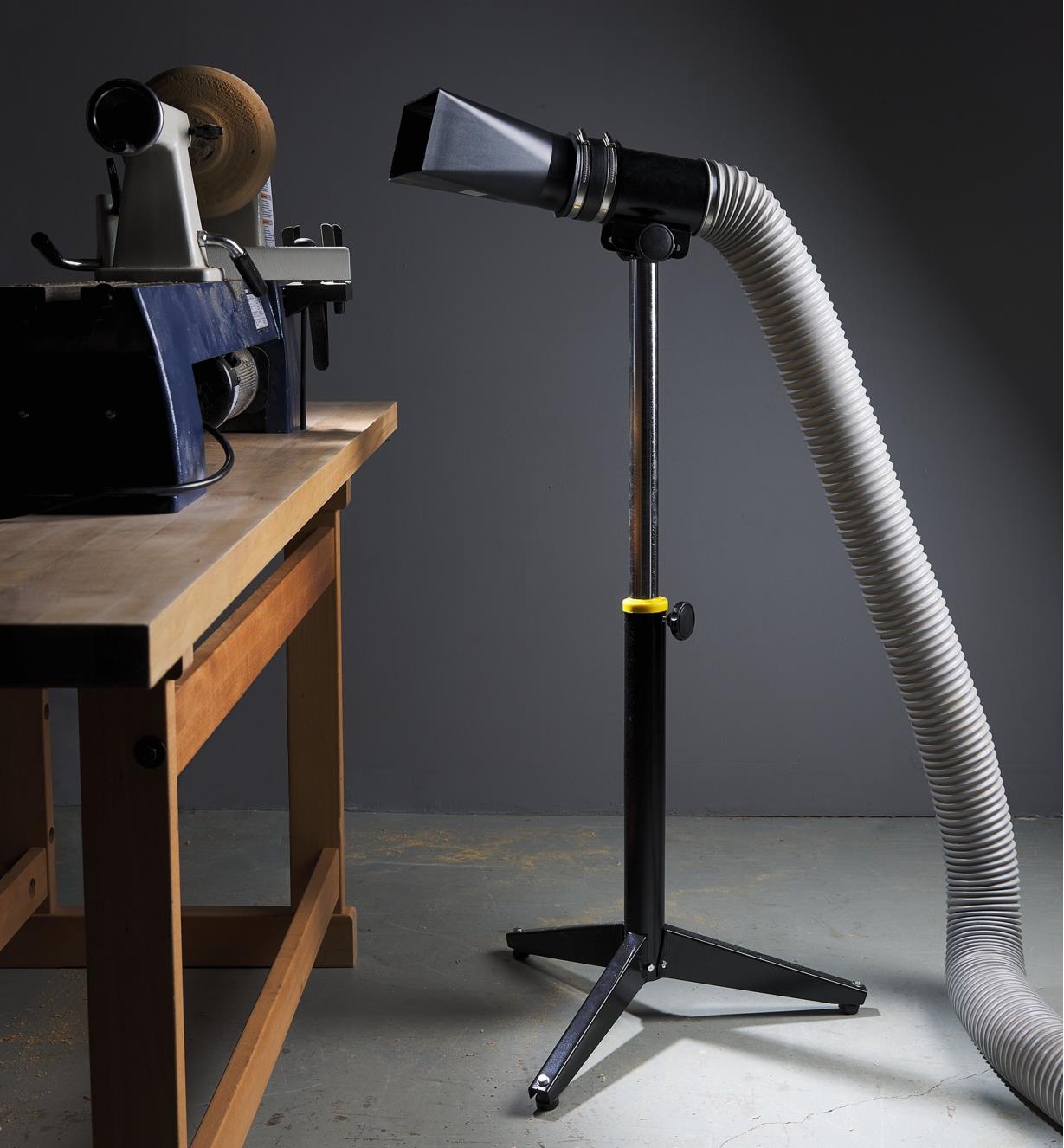 A stand with a dust hood connected to a hose next to a workbench and lathe