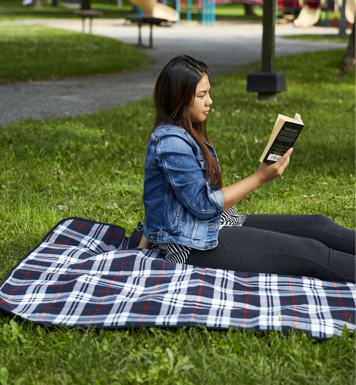 A person reads a book while sitting on the tartan outdoor lined blanket