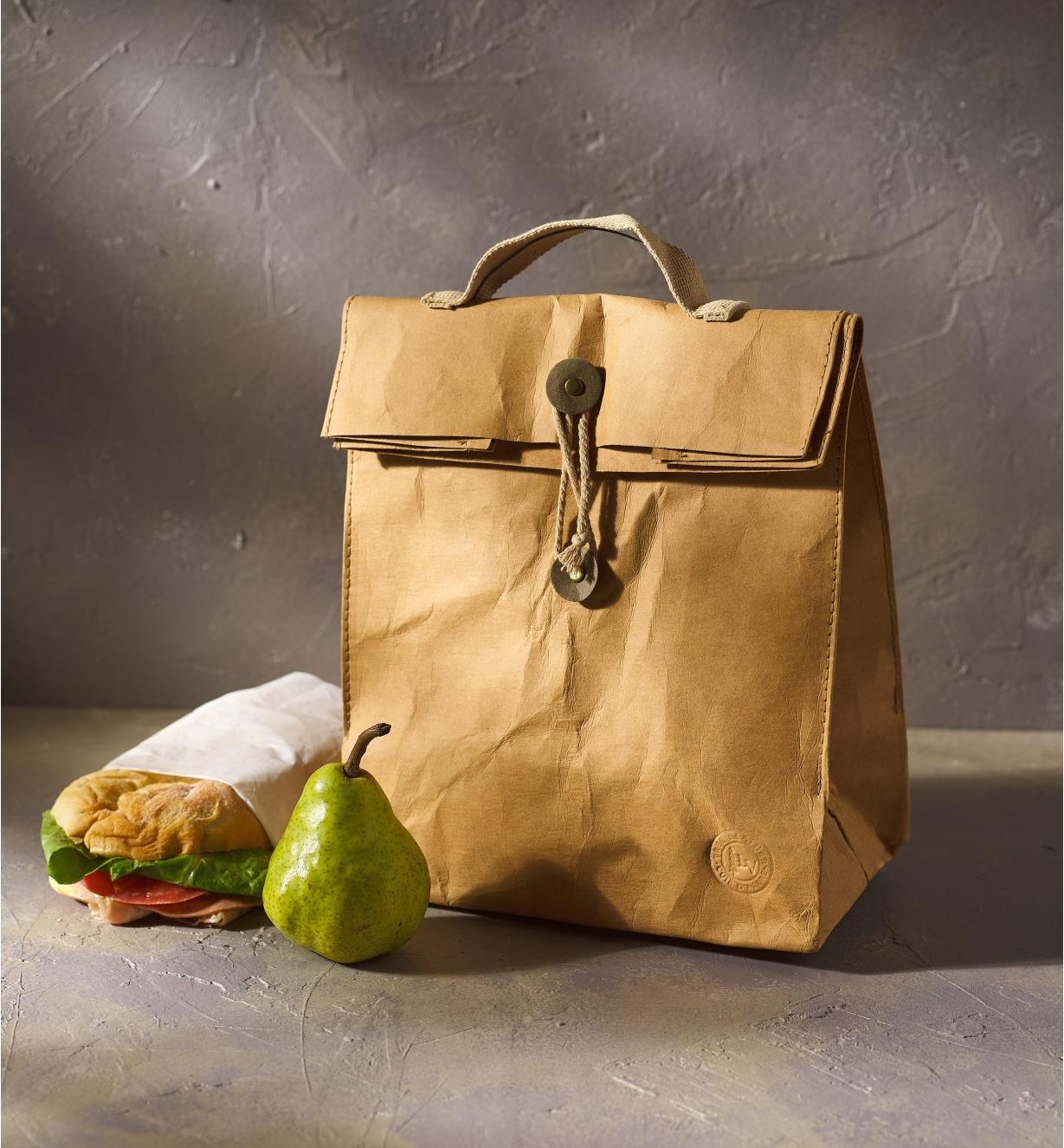 A sandwich and a pear outside a closed tree leather lunch bag