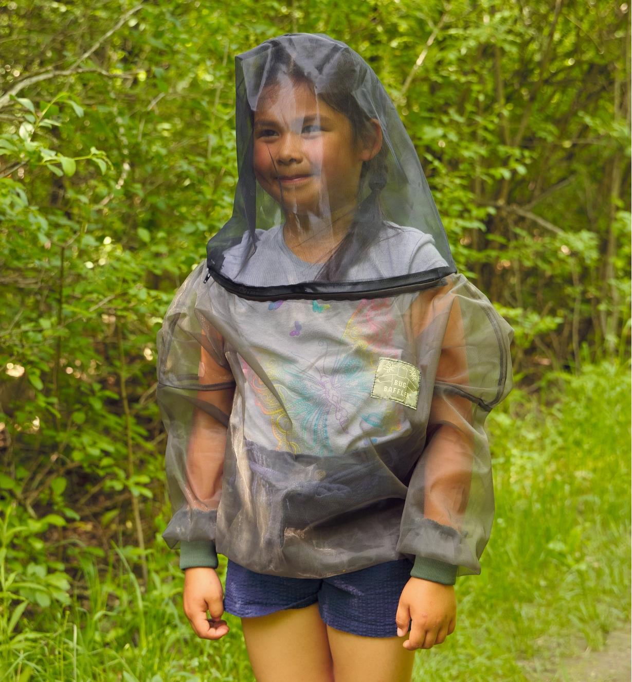 A child wears a bug-protection shirt in a woodland setting