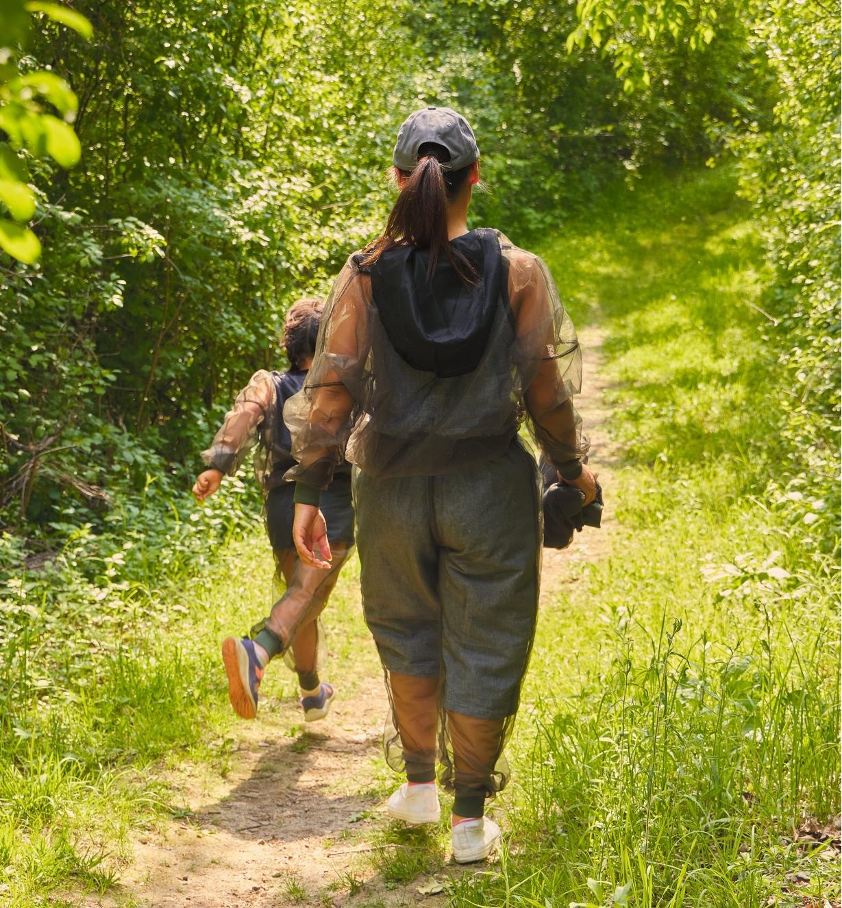 A rear view of a woman and a child wearing bug-protection clothing on a hiking trail