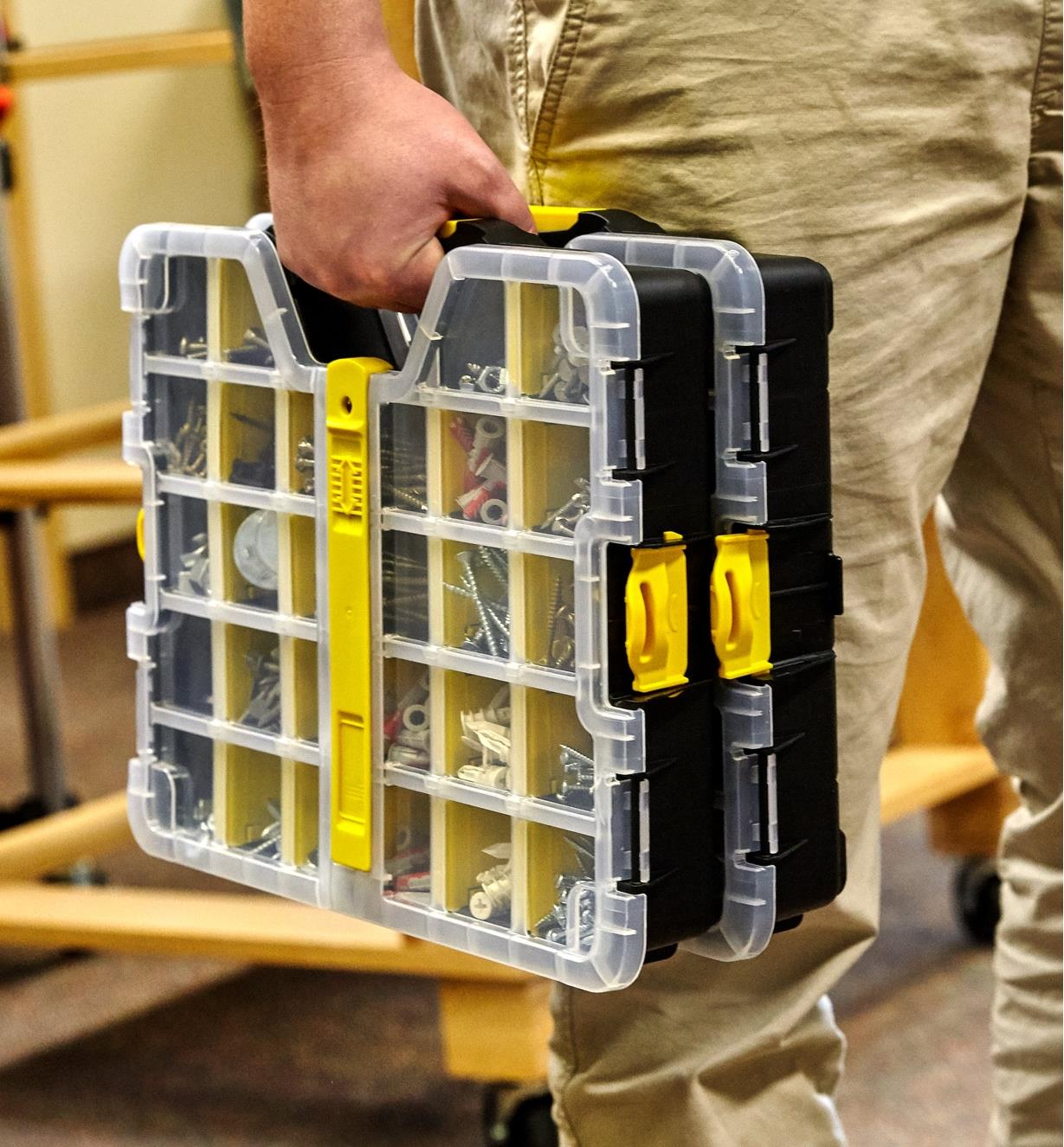 A person carries two 11" × 14" cases clipped together and filled with screws and drywall anchors