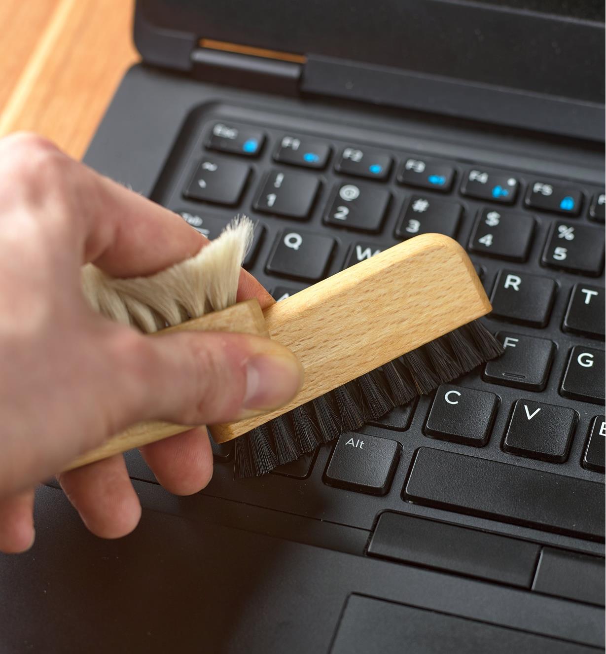 Using the black bristles of the detail dusting brush to clean a laptop keyboard