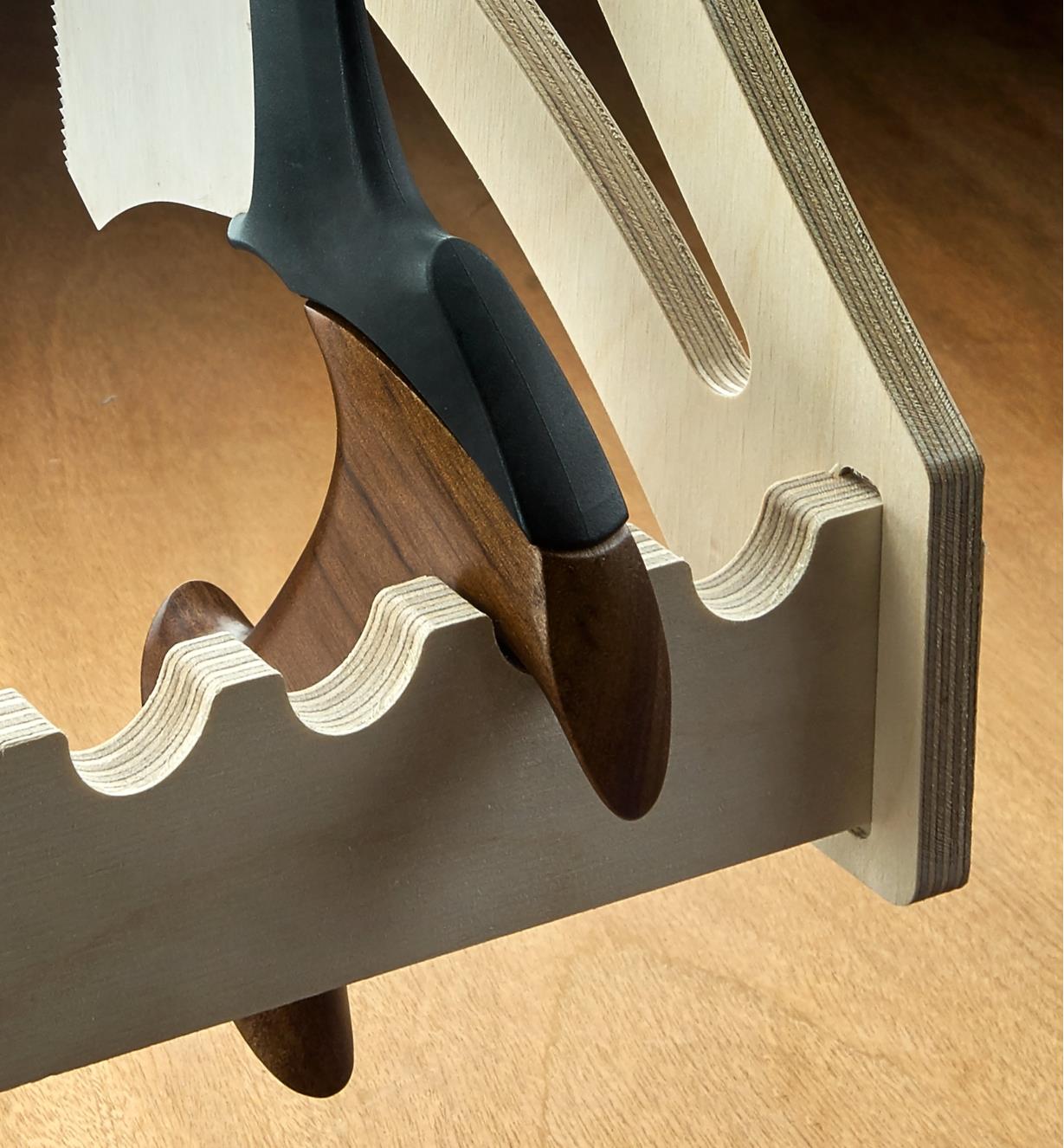 A close-up of a saw handle resting in one of the rounded cutouts at the bottom of the four-saw till