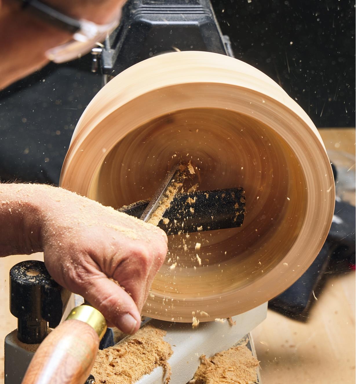 A gouge cutting the inside of a bowl blank while being supported on a curved rest