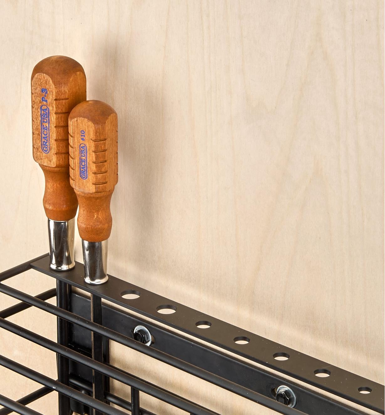 Screwdrivers stored in holes set in a bar at the back of a wall-mount tool storage rack