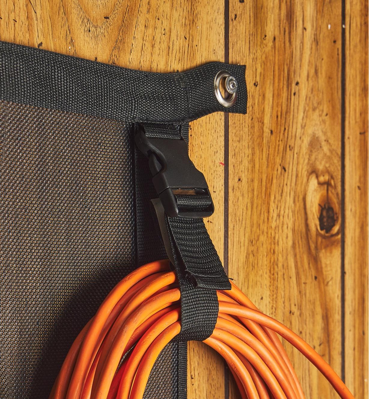 A strap on a hanging organizer is holding a coiled, orange extension cord.