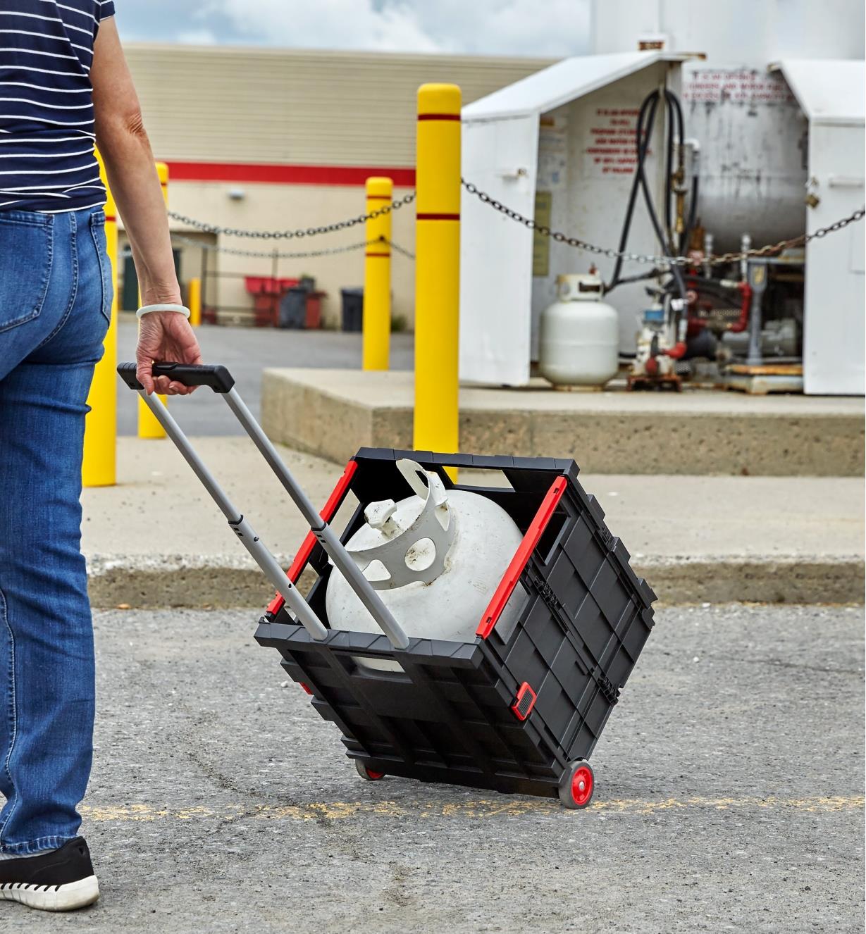 A person at a propane filling station pulls a collapsible cart containing a 20 pound propane tank
