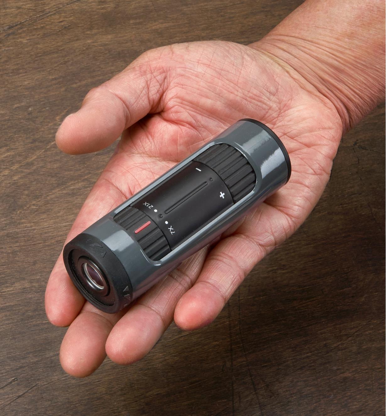 A man holds a zoom monocular in the palm of his hand