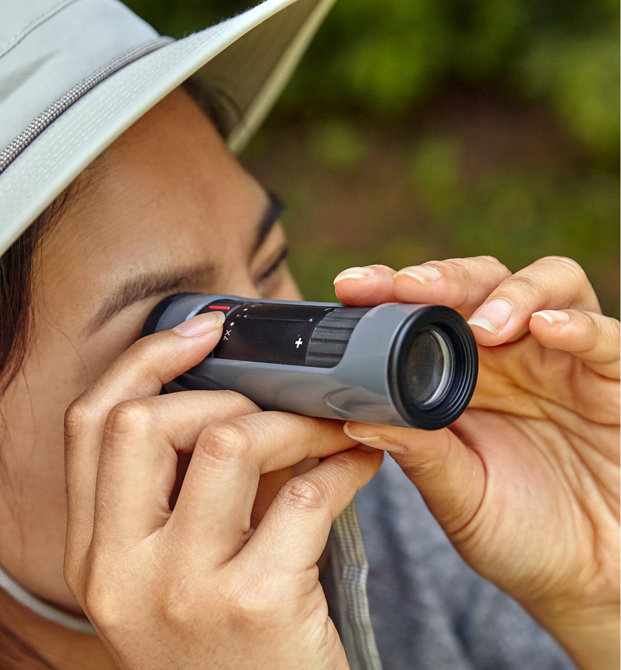 A woman holds a zoom monocular to her eye while adjusting the zoom and focus dials