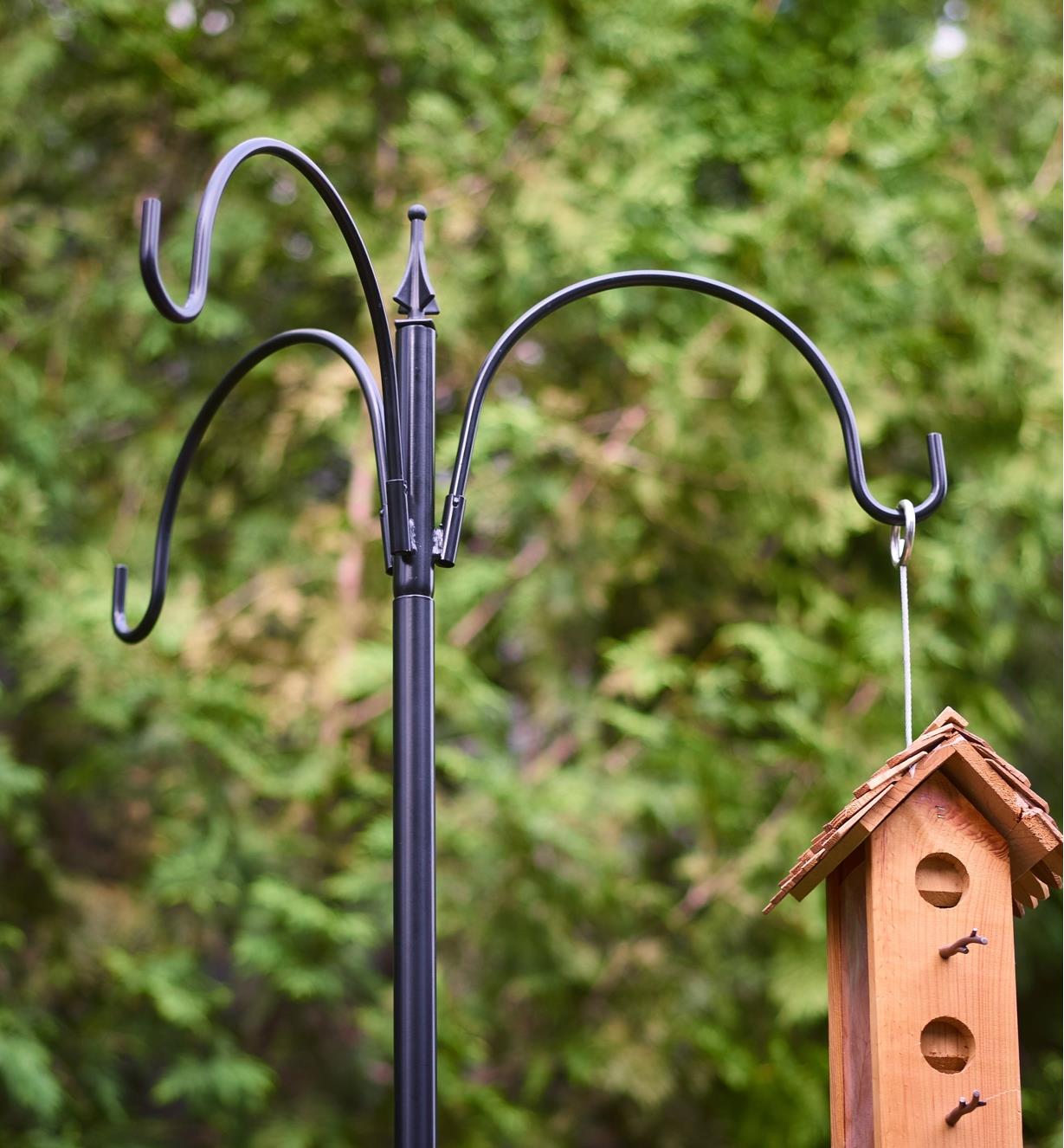 A birdhouse hanging from a three-arm garden pole