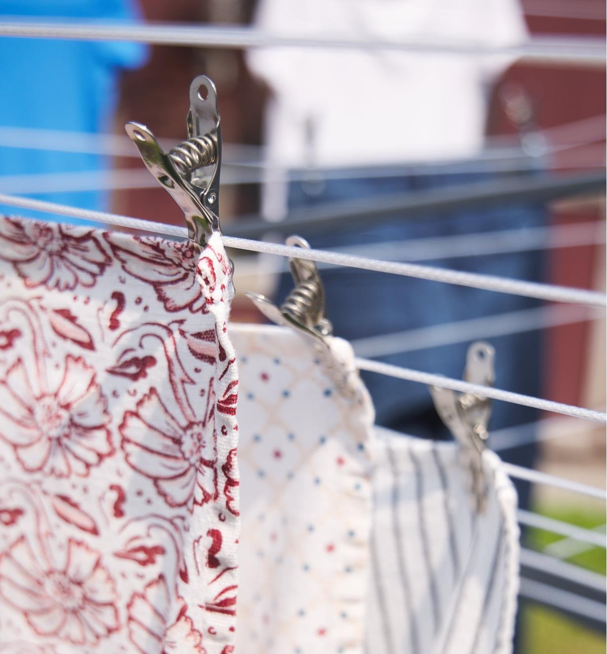A steel clothespin holds a floral print towel to a clothesline.