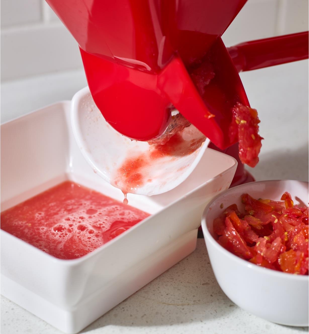 Tomato press sits on a counter with pulp and juice running into the catch bowls