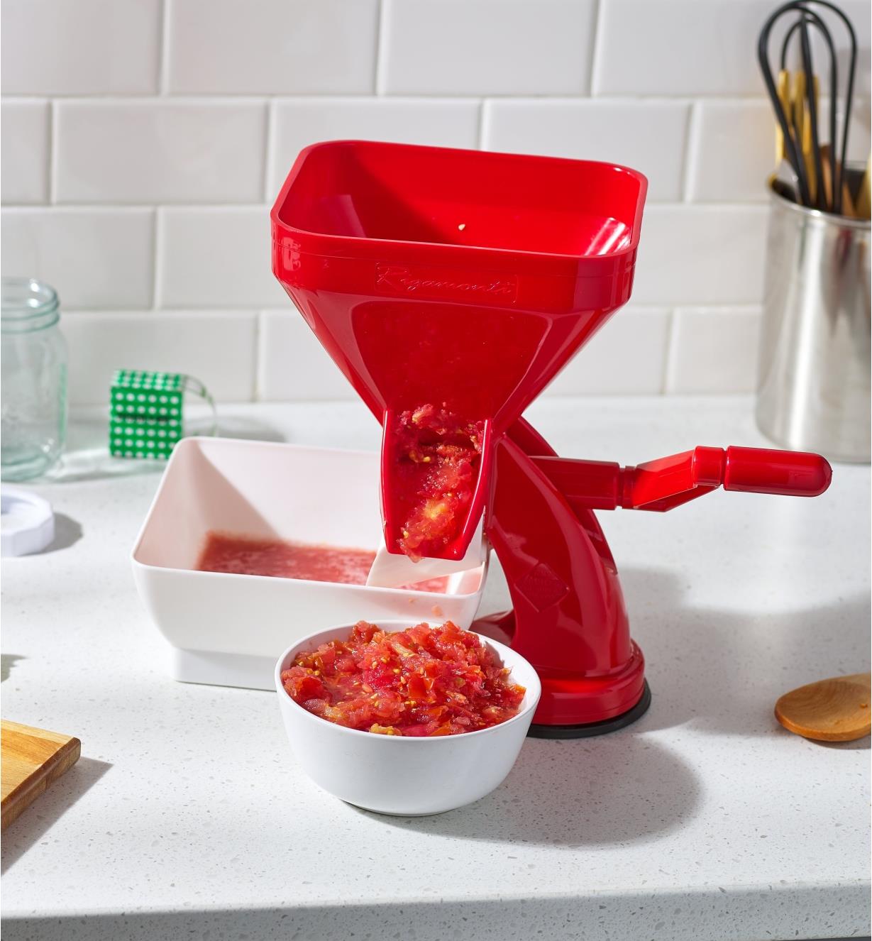 Tomato press sits on a counter with skins and seeds running into a bowl