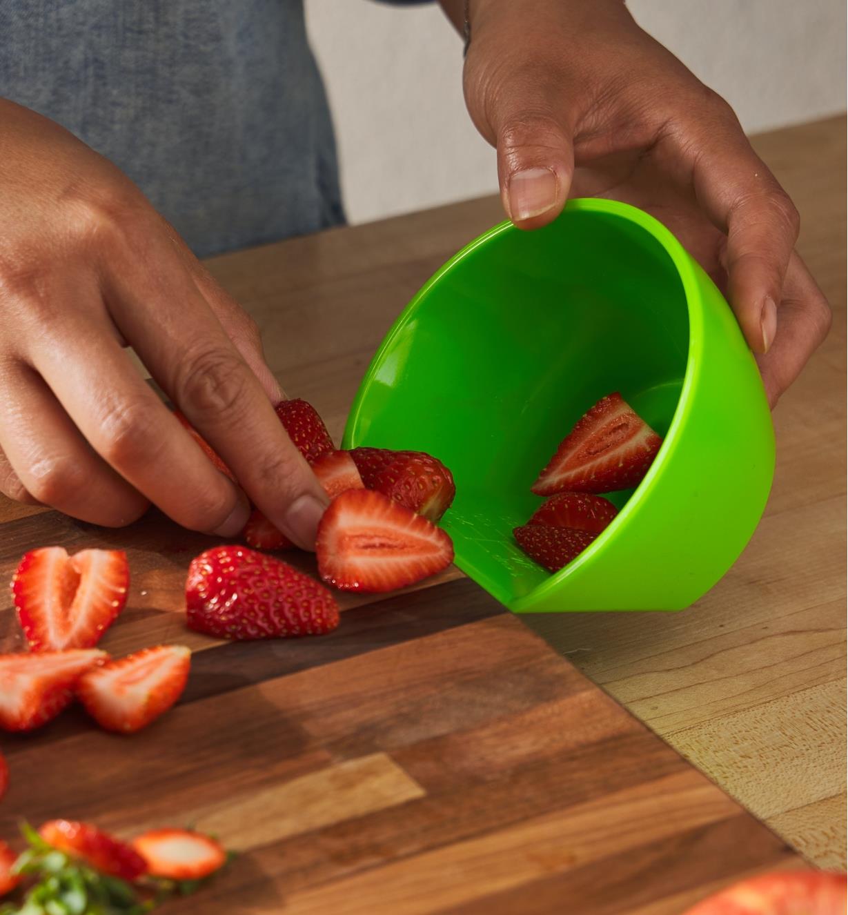 Pushing fruit pieces into a scoop measuring bowl placed at the lip of a cutting board