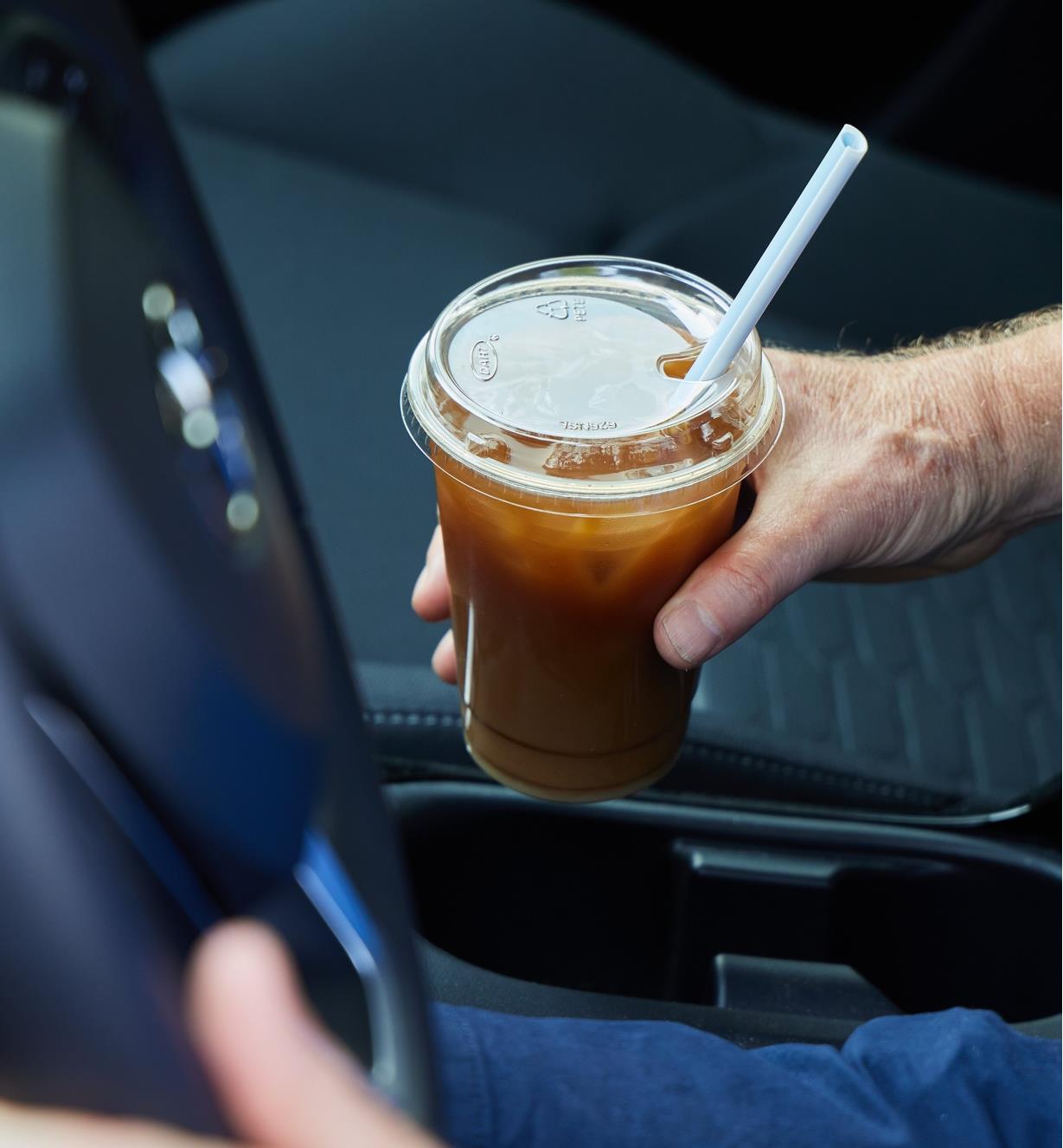 A person in a car holding a plastic cup with a lid and a slider straw in it