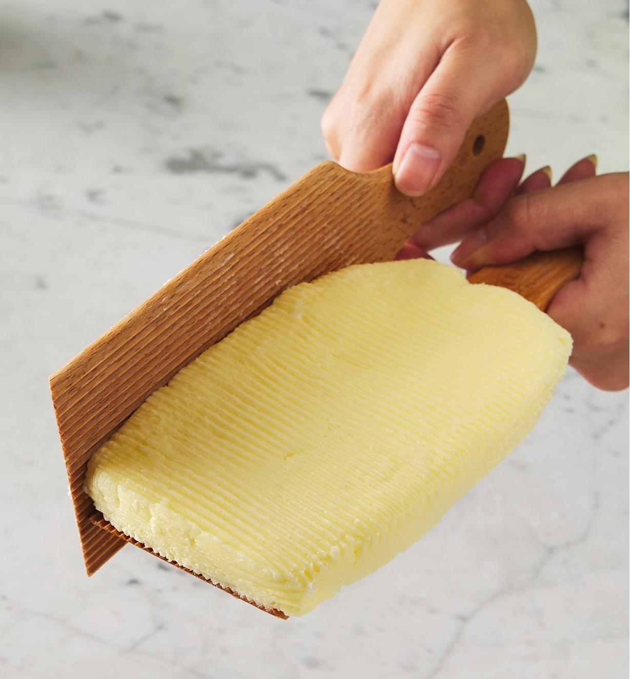 Butter on a paddle being molded into a brick with the other paddle