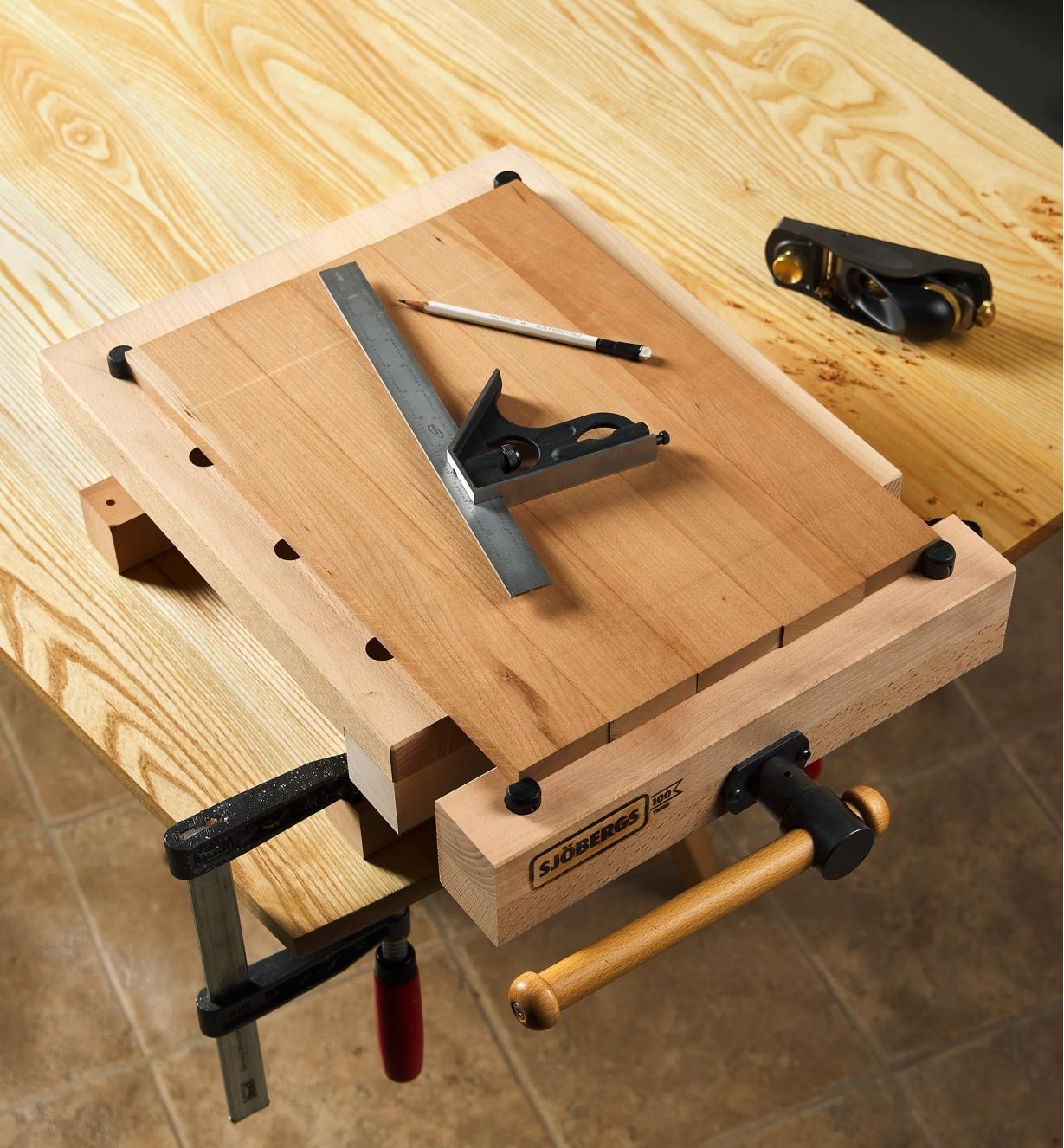 A workbench with a workstation clamped to it with a board and combination square