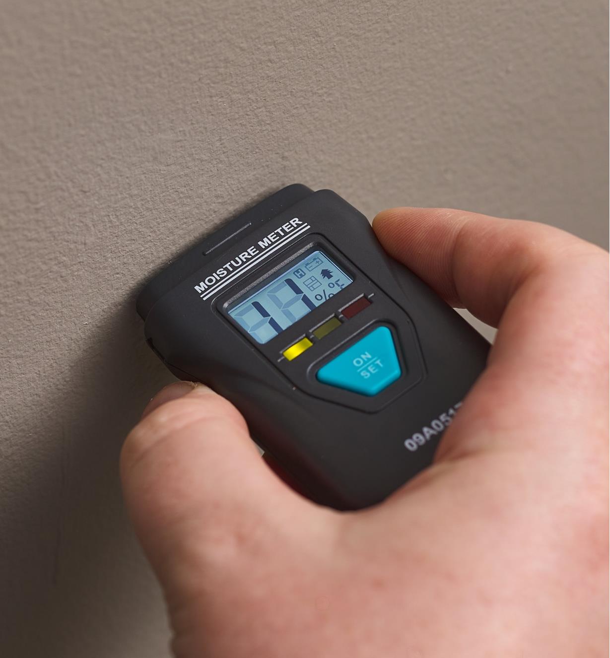 Personne mesurant l’humidité dans un matériau à l’aide d’un hygromètre numérique indiquant onze pour cent d’humidité avec l’indicateur lumineux DEL vert allumé.