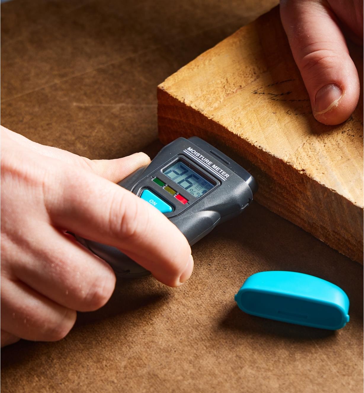 The Digital Moisture Meter being pressed into wood, showing a high reading and red LED indicator.